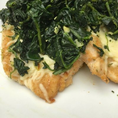 Close up of breaded chicken topped with mozzarella and garlic spinach.