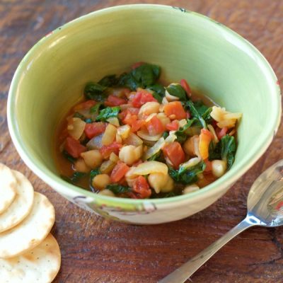 Bowl of boiled chickpeas mixed with onions, diced tomatoes, chopped spinach, and golden raisins.
