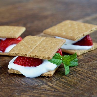Two graham cracker sandwich stuffed with yogurt, strawberries, and a sprig of basil.